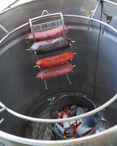 Salchichas cocinándose sobre brasas en barbacoa vertical.