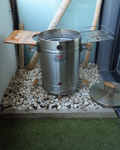 Horno metálico en un jardín con piedras.